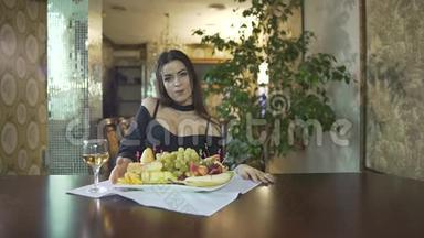 一位身着黑色礼服、乳沟般的年轻女子独自在<strong>高档餐厅</strong>的餐桌上吃水果、葡萄